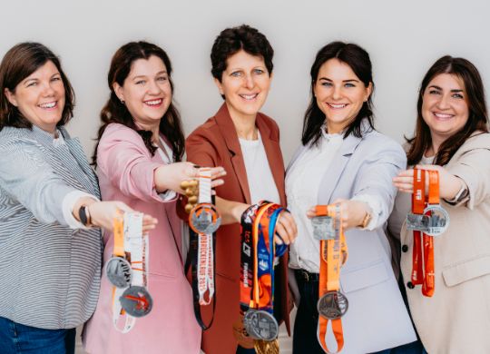 Das Bild zeigt fünf Personen (das Team), mit Medaillen in der Hand.